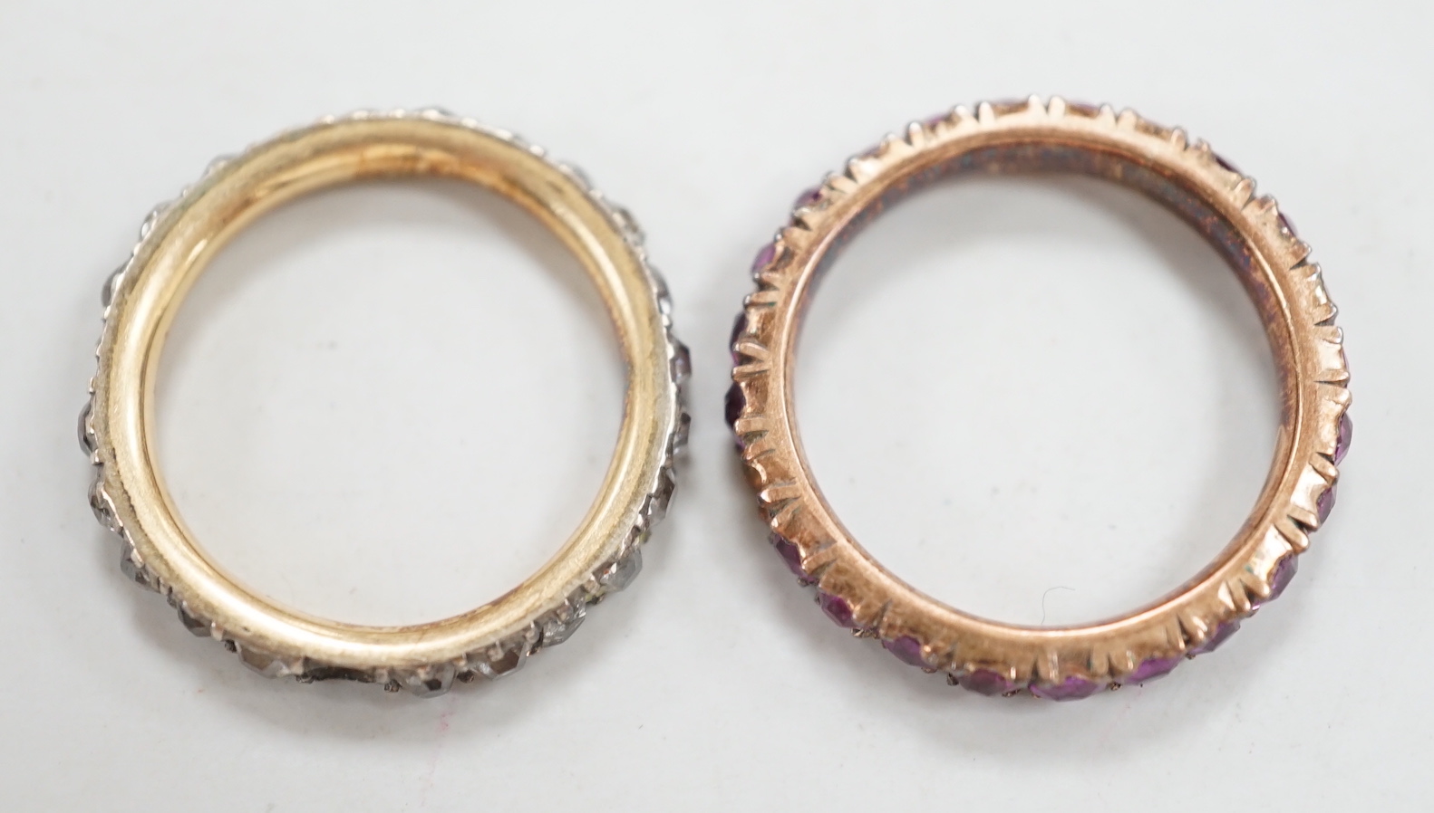 An antique yellow metal and diamond set full eternity ring (stone missing), size L and a similar pink stone set eternity ring.